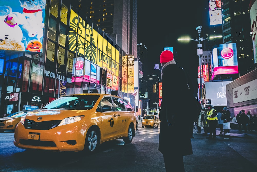 uomo che indossa un cappotto nero in piedi vicino a un taxi giallo