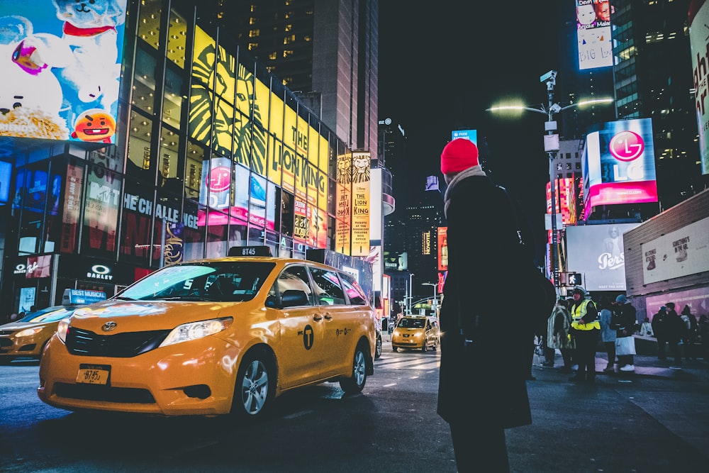 Mann im schwarzen Mantel steht neben gelbem Taxi