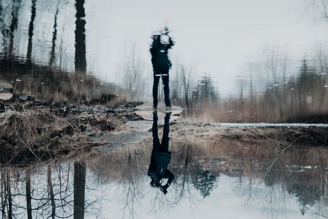 water reflection of a person holding camera standing near pond