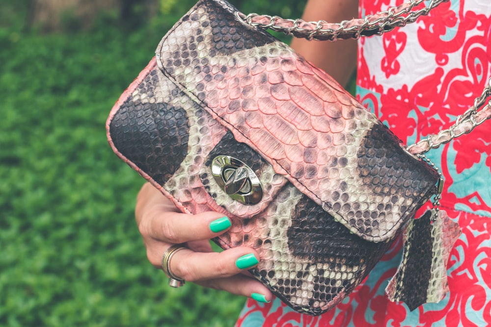 person holding gray and black snakeskin-printed bag