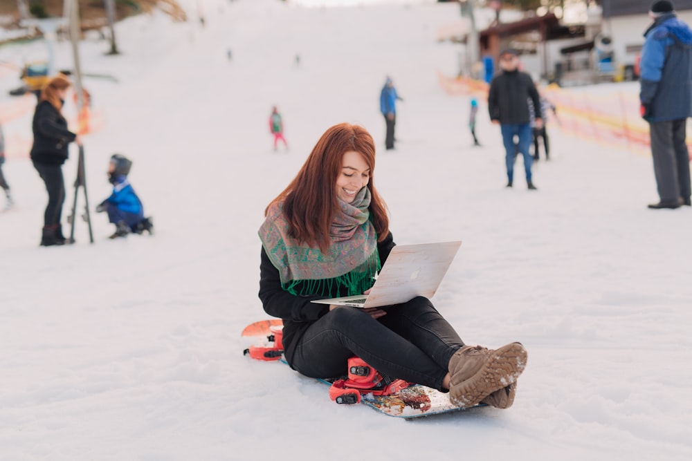 woman sitting on snowboard using MacBook Pro