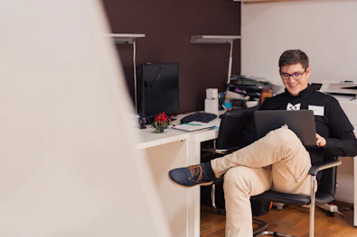 A friendly small business owner smiling while using a laptop in a cozy shop setting.