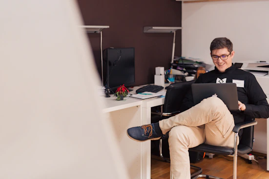 A person happily managing their budget with a laptop and notes on a cozy desk