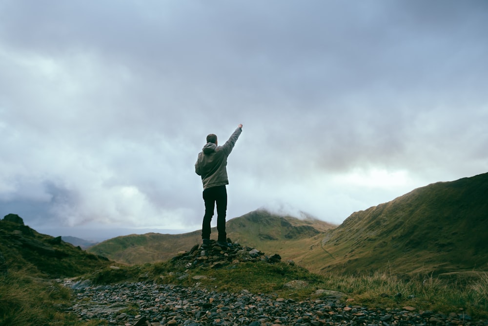 man standing on rocks near mountains pointing sky during daytime