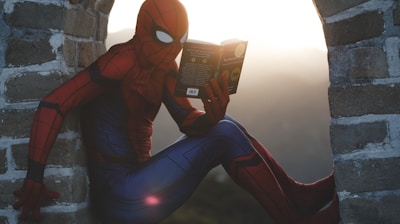 Spider-Man leaning on concrete brick while reading book