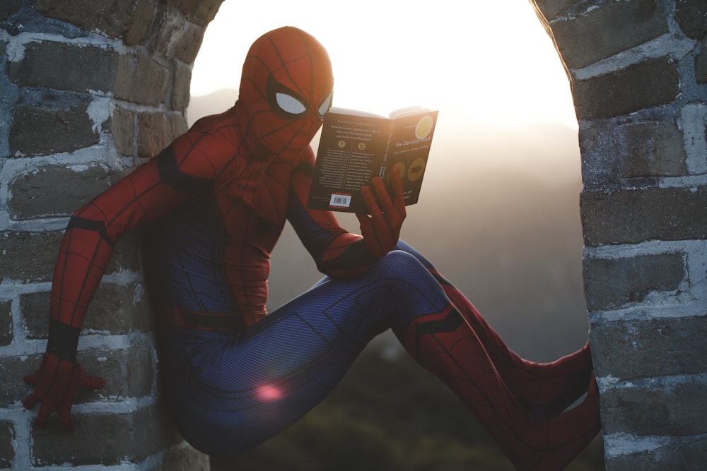 Spider-Man leaning on concrete brick while reading book