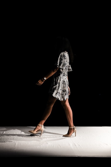 A striking black-and-white runway shot capturing a model mid-stride under dramatic lighting.