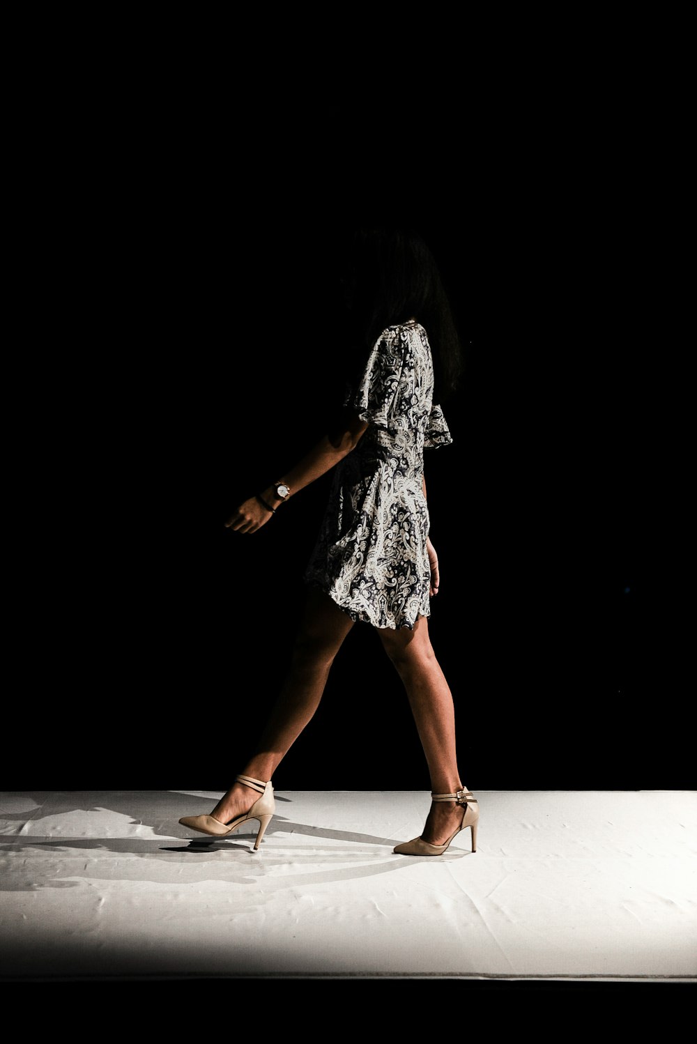 woman wearing black and white floral dress walks inside dark room