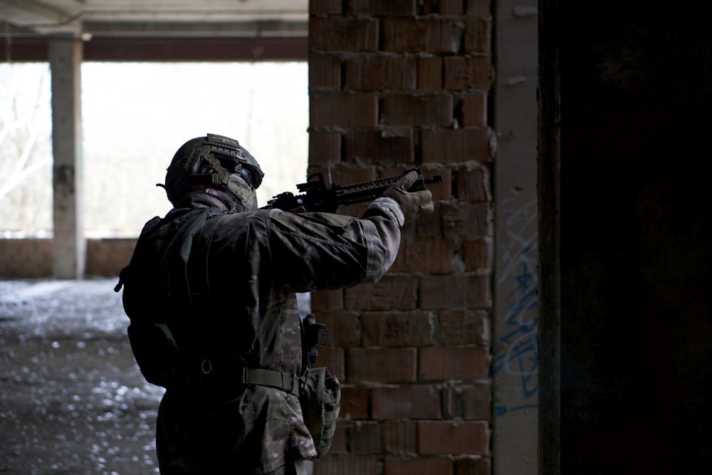man holding rifle beside wall