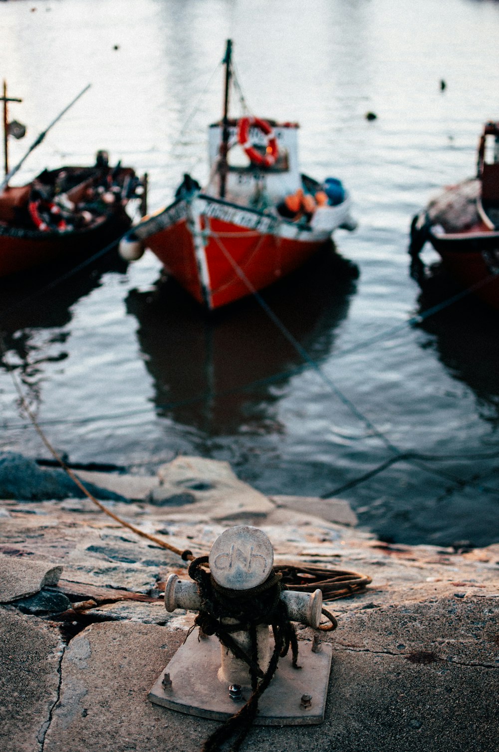 selective focus photo of three red boats on body of water view from gray pavement