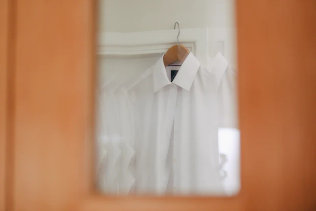 Une chemise blanche immaculée suspendue à un cintre, fond clair et lumière douce