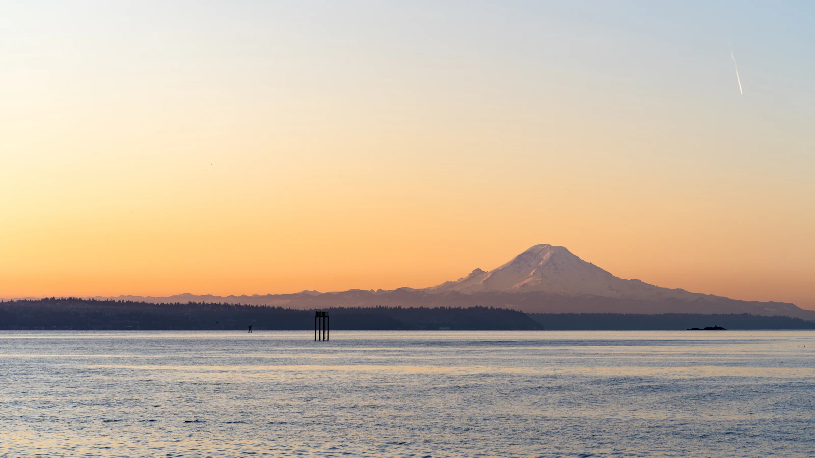 Mount Rainier silhouetted above the calm waters of Puget Sound at an orange-and-pink sunset