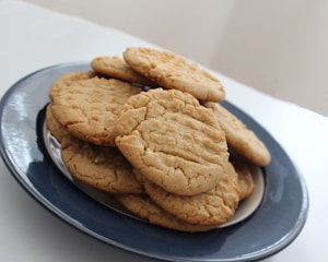 A stack of homemade peanut butter cookies arranged on a dark blue ceramic plate with a white interior. The cookies have a rustic, textured appearance, suggesting they are freshly baked.