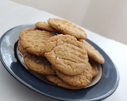A stack of homemade peanut butter cookies arranged on a dark blue ceramic plate with a white interior. The cookies have a rustic, textured appearance, suggesting they are freshly baked.