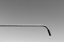 A minimalist image featuring a single metal pipe with a slight bend towards the right end. The background is a smooth gradient transitioning from dark gray at the top to light gray at the bottom, emphasizing the simplistic and abstract nature of the composition.