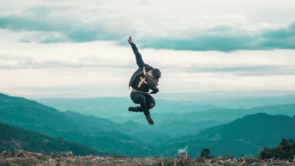 photo of man in jacket and pants jumping while posing