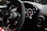 A close-up view of a car's interior focusing on the steering wheel and dashboard. The steering wheel features a prominent brand logo at the center, and nearby, a prominent start/stop button is visible. The dashboard displays modern digital gauges and controls with a sleek design.