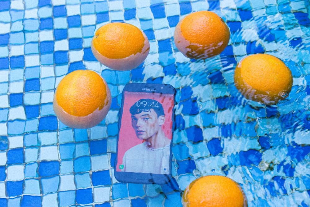 Fünf orangefarbene Früchte und ein schwarzes Smartphone auf dem Wasser
