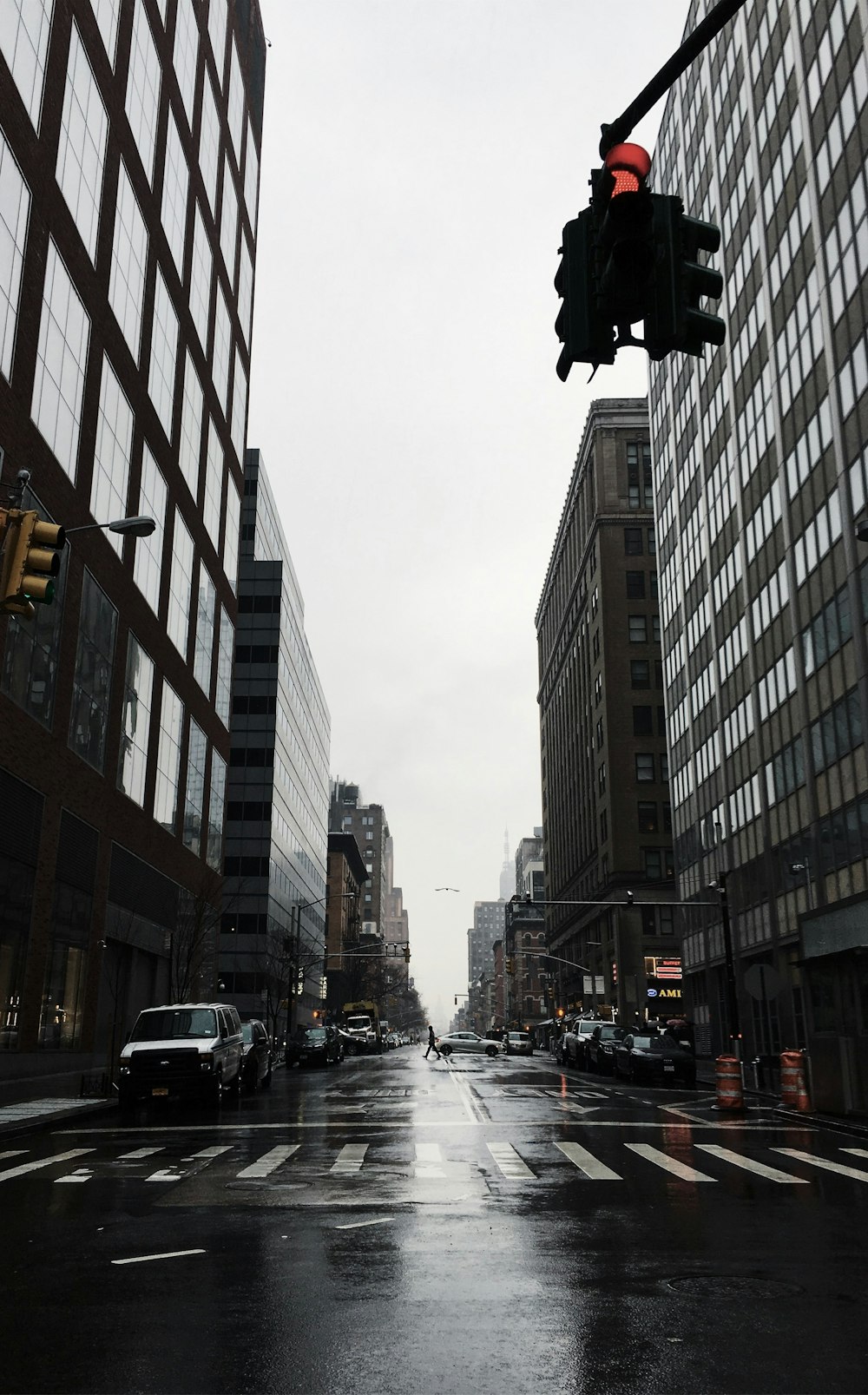 vehicles on grey wet road between buildings during daytime