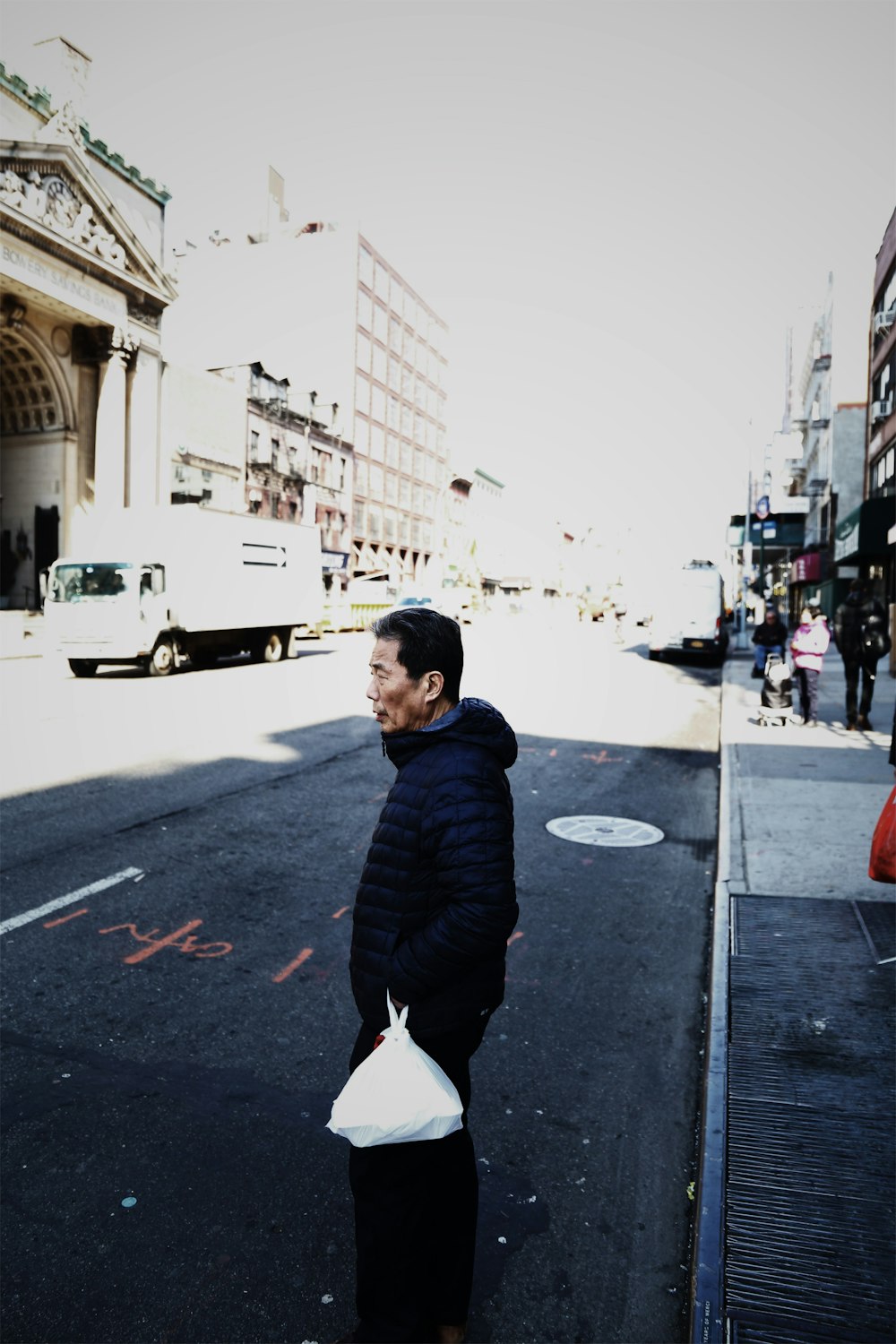 man carrying plastic bag while standing on roadway