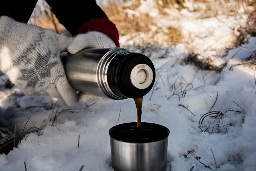 person holding vacuum flask putting brown liquid on cup