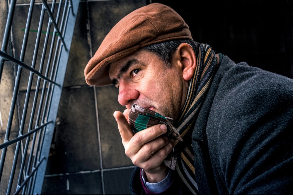 man in blue coat and brown cap near a blue metal mesh gate