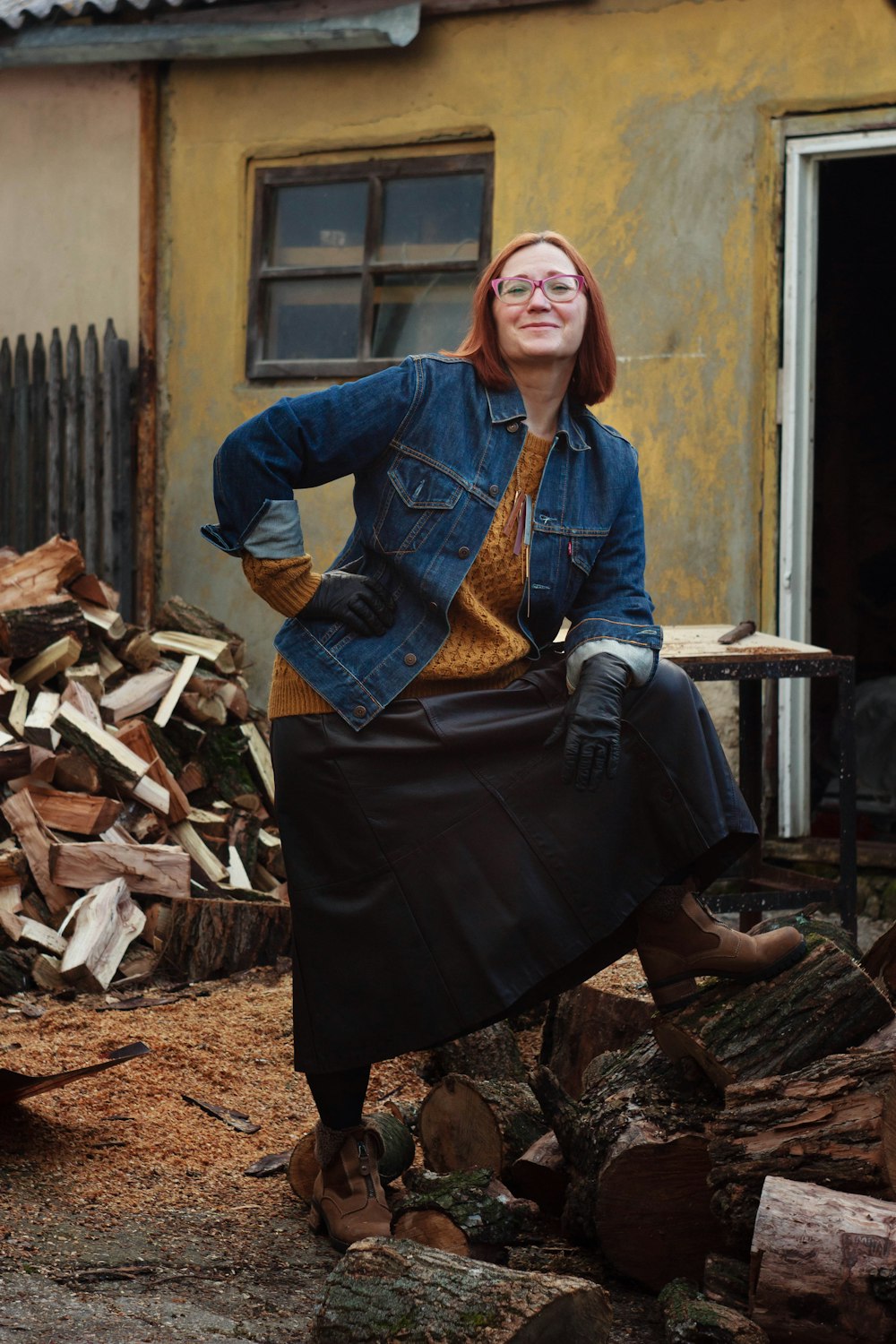 brown haired woman in blue denim jacket standing near firewoods