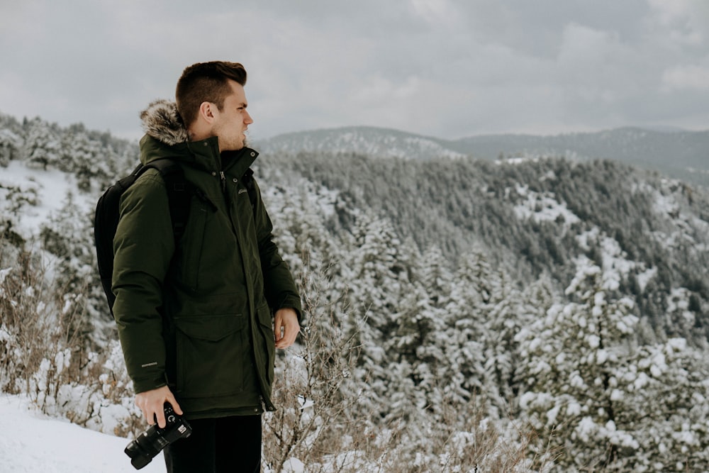 photo of man wearing green jacket holding DSLR camera