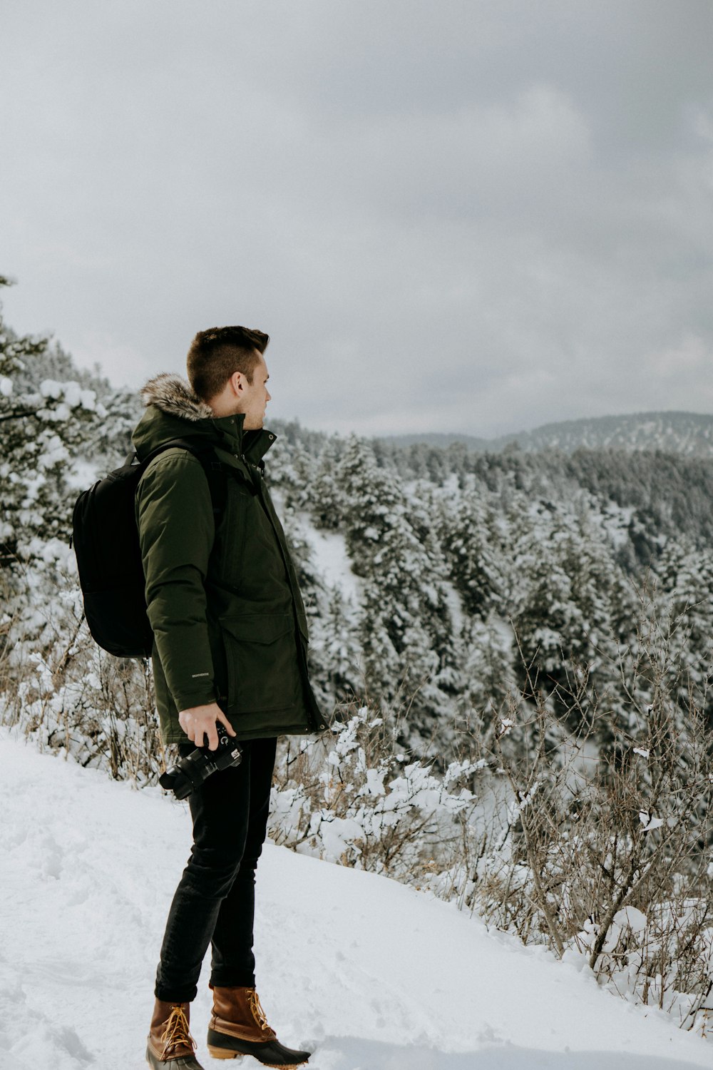 man standing on snow looking at trees under cloudy sky