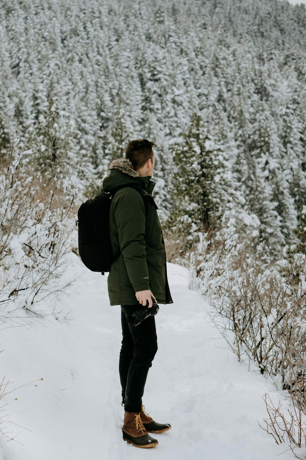 hombre de pie sobre la nieve mirando en los árboles durante el día