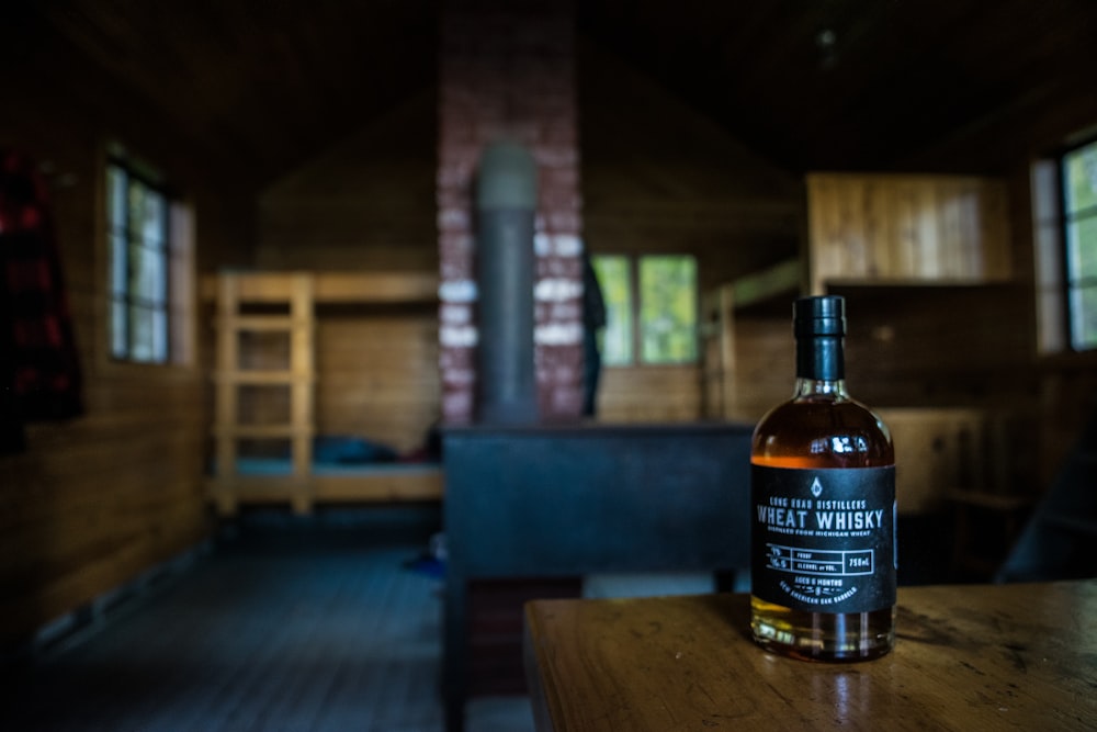 fotografia a fuoco superficiale della bottiglia di whisky di frumento sul tavolo di legno marrone all'interno della casa