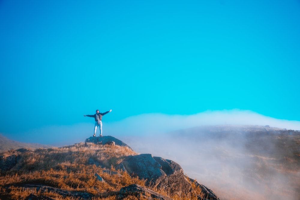 personne debout sur la montagne brune et noire sous le ciel bleu pendant la journée