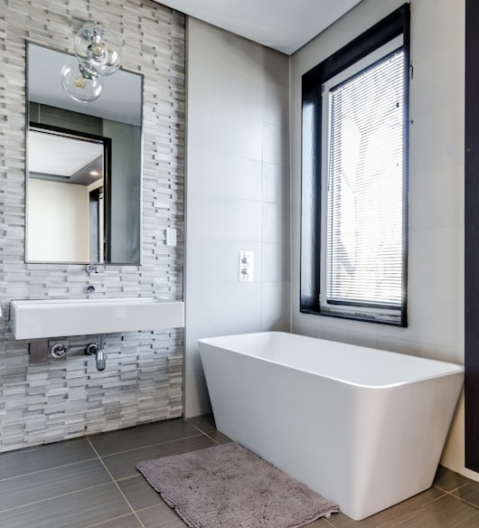 white ceramic bathtub near white framed window