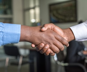 close up of a black hand and white hand shaking, both wrists show smart shirt cuffs