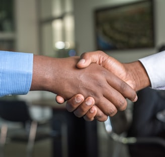 close up of a black hand and white hand shaking, both wrists show smart shirt cuffs