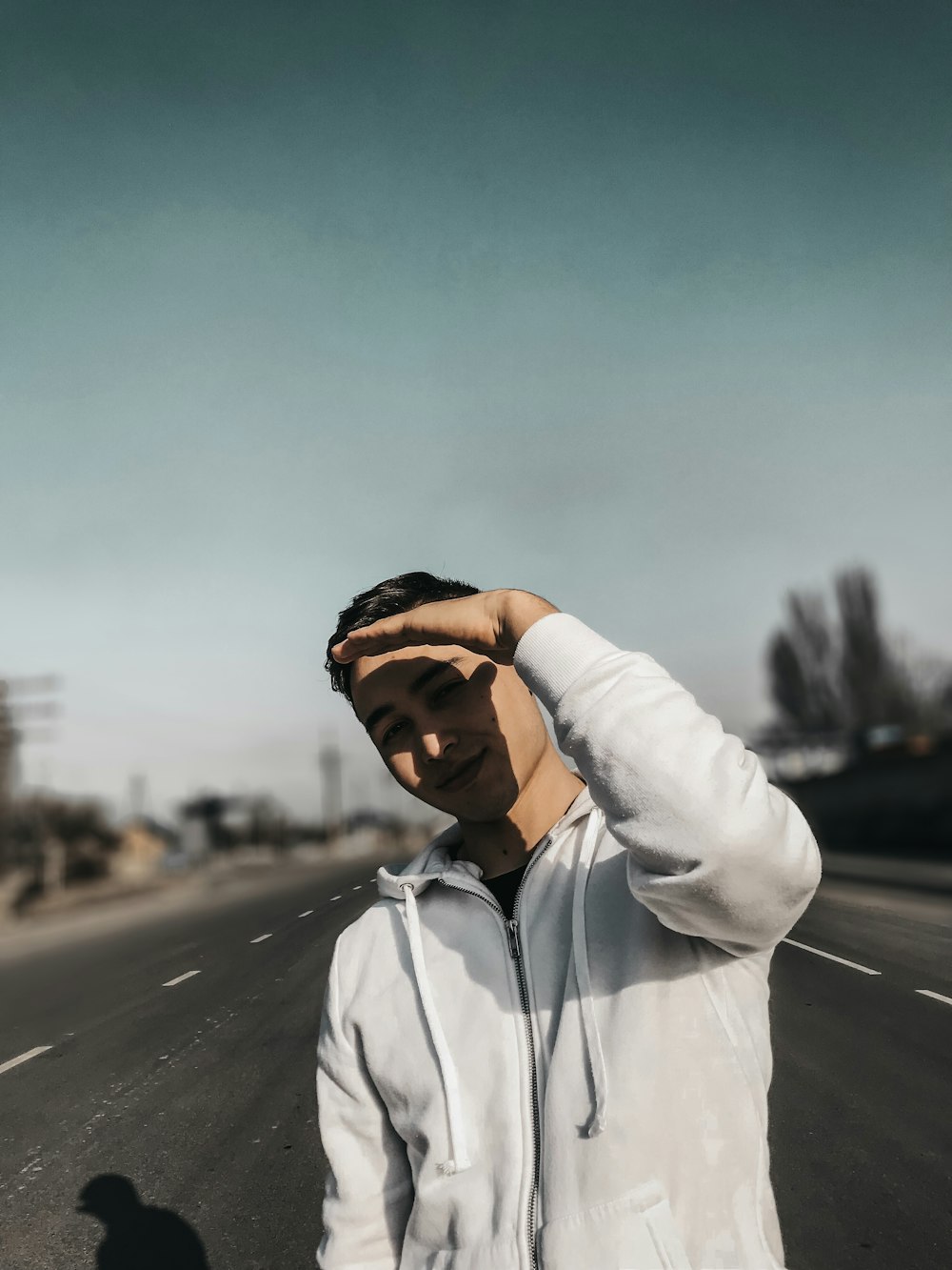 tilt-shift lens photography of man shading his eyes from sun while standing on blacktop road during daytime