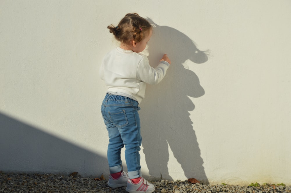 niño tocando la pared pintada de blanco durante el día