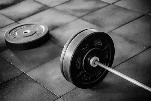 A close-up of a barbell with red and black weight plates resting on a gym floor.