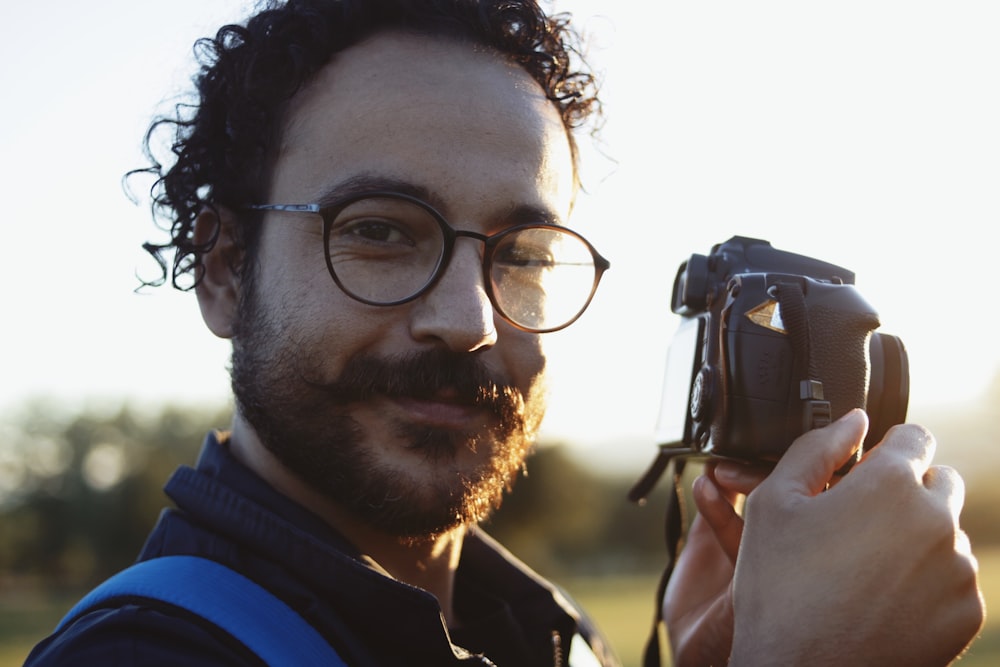 homme portant des lunettes tenant un appareil photo reflex numérique