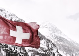 white and red cross flag in front of snow covered mountains
