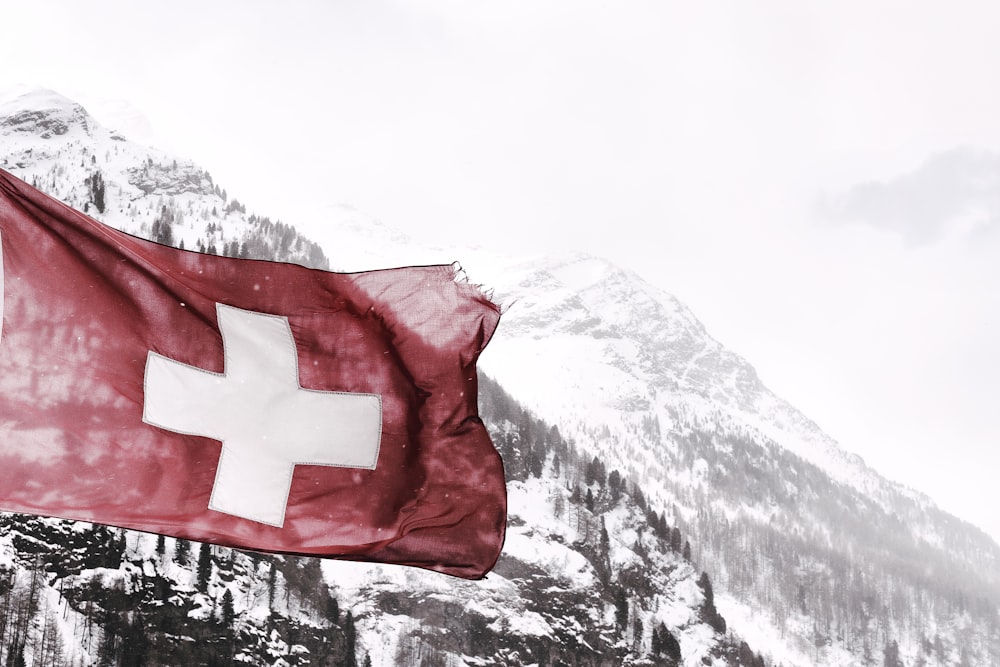 white and red cross flag in front of snow covered mountains