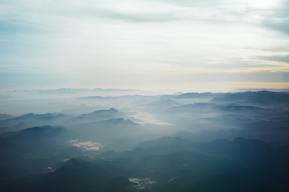 Fotografía aérea de montañas azules rodeadas de niebla bajo el cielo blanco durante el día