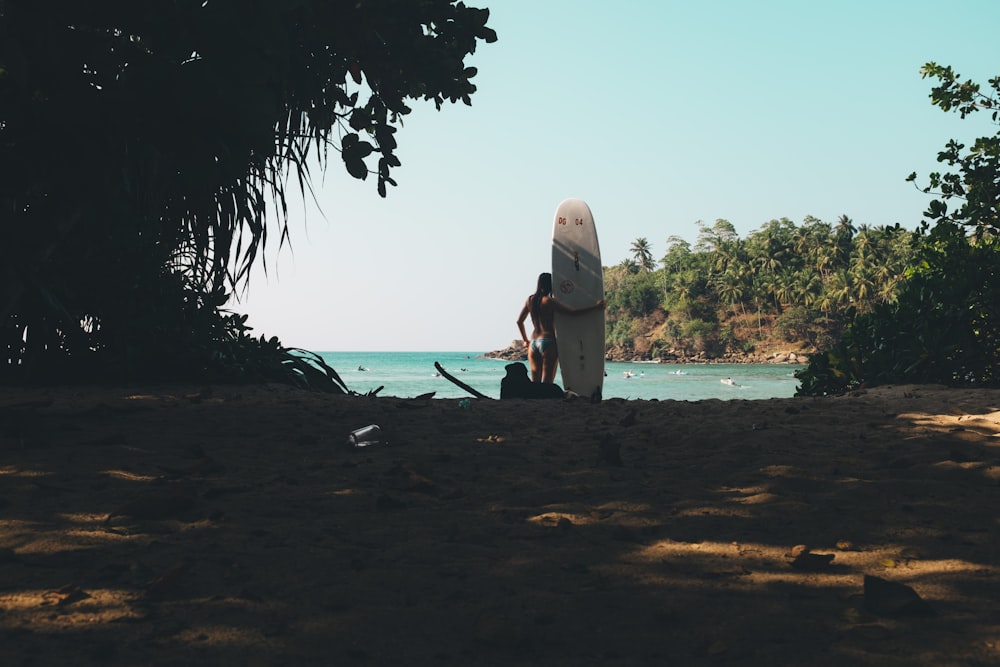 personne tenant une planche de surf blanche debout sur le bord de la mer pendant la journée