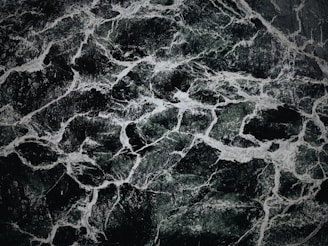 The image displays an intricate pattern of dark green and black marble with white veining. The texture appears smooth and polished, with the veins creating a natural, abstract design across the surface.