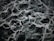 The image displays an intricate pattern of dark green and black marble with white veining. The texture appears smooth and polished, with the veins creating a natural, abstract design across the surface.