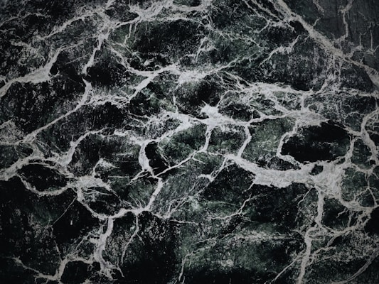 The image displays an intricate pattern of dark green and black marble with white veining. The texture appears smooth and polished, with the veins creating a natural, abstract design across the surface.