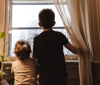 boy and girl standing near window looking outside