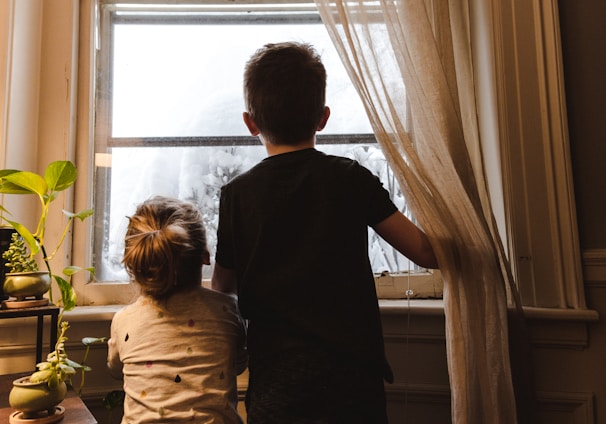 boy and girl standing near window looking outside