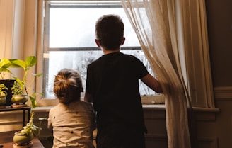 boy and girl standing near window looking outside