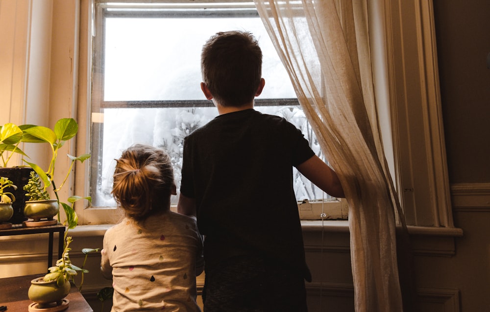 garçon et fille debout près de la fenêtre regardant à l’extérieur